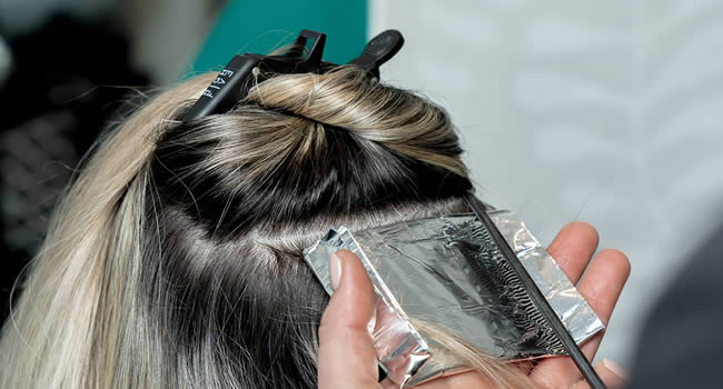 Friseur trägt Haarfarbe auf und deckt sie mit Folie ab.